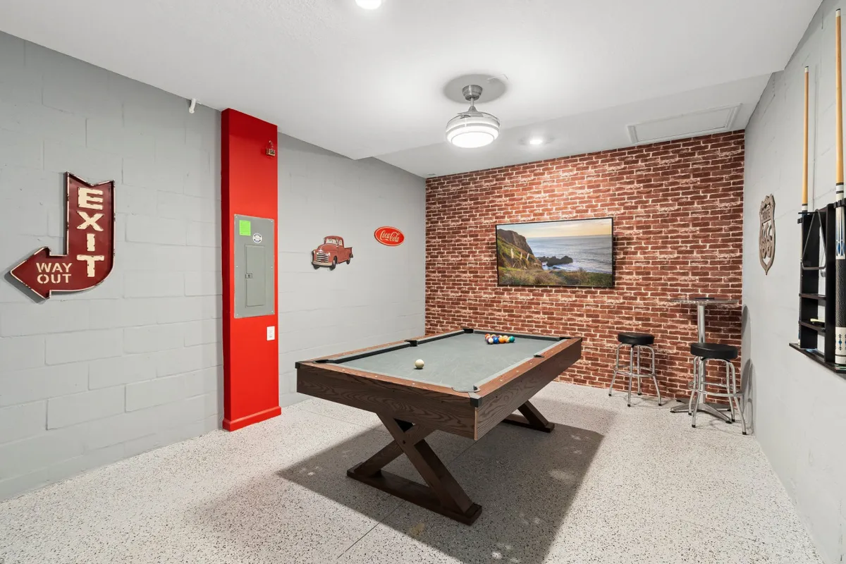 A playful interior scene featuring a pool table set against a brick wall with a vintage Coca-Cola sign and colorful artwork, evoking a family-friendly game room. The relaxed setting suggests an ideal spot for indoor fun and bonding moments.