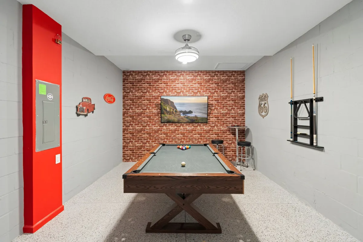 This image captures a vibrant game room featuring a pool table as the central focus, set against a backdrop of a brick wall, colorful artwork, and vintage decorations. The room exudes a casual and fun atmosphere, perfect for friendly competitions and socializing with friends or family.