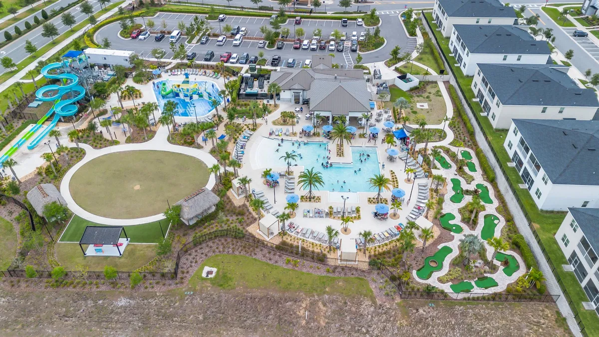 This vibrant exterior image showcases a large resort-style swimming pool surrounded by palm trees, with prominent water slides, a play area, a visible mini golf course, and ample lounge chairs. The lively scene is set in bright daylight, with families and children enjoying the multiple amenities.
