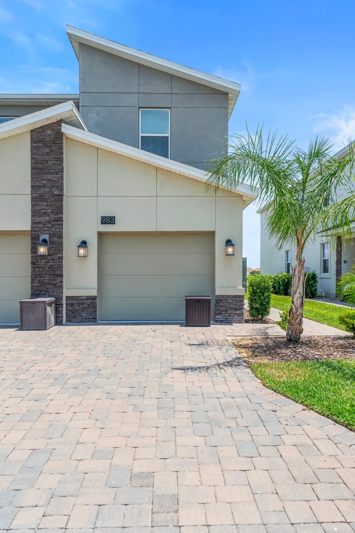 A welcoming exterior with modern architecture, a paved driveway, and lush landscaped gardens featuring palm trees. There is space for outdoor gatherings, morning coffee on the patio, and children playing in the garden.