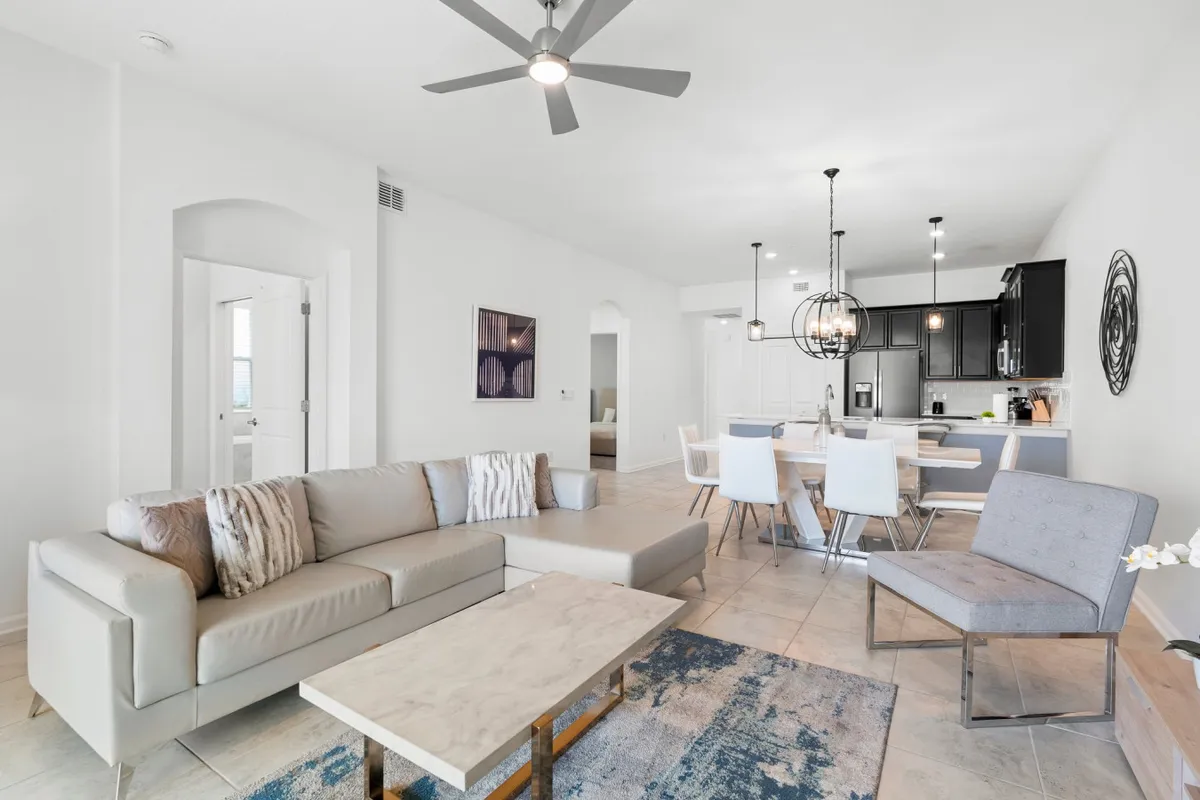 This image captures a welcoming open-plan space featuring a modern sofa, a stylish coffee table, the adjoining dining area, and the entrance to the kitchen. Decorative wall art adds a touch of personality. The layout clearly conveys the seamless transition between living, dining, and kitchen spaces, ideal for socializing, family meals, and shared activities.