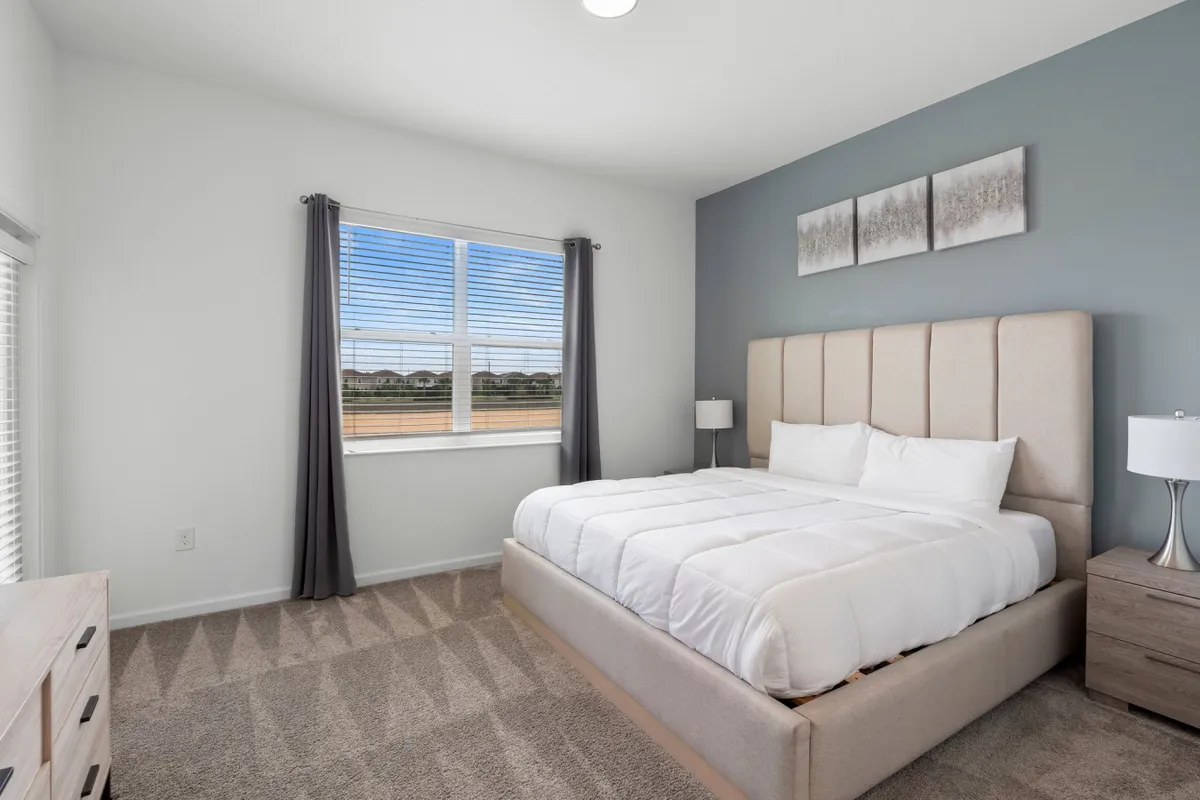 A serene bedroom with a comfortable bed, window allowing natural light, a nightstand, and decorative artwork. The space exudes tranquility and is ideal for rest and relaxation.