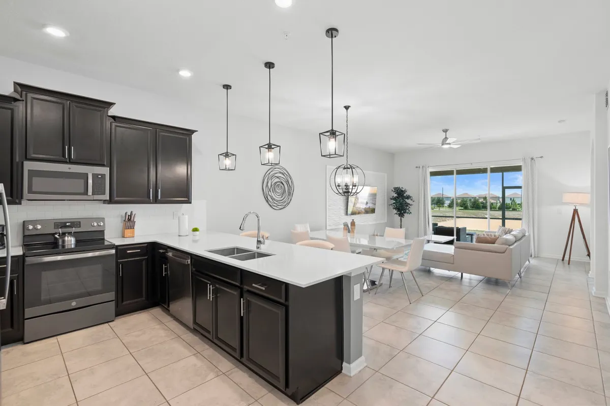 A spacious and modern kitchen with a large island in the center, featuring stainless steel appliances, elegant light fixtures, and a dining area with large windows that let in natural light. The kitchen island serves as both a prep space and a gathering spot, reinforcing the open-concept design.