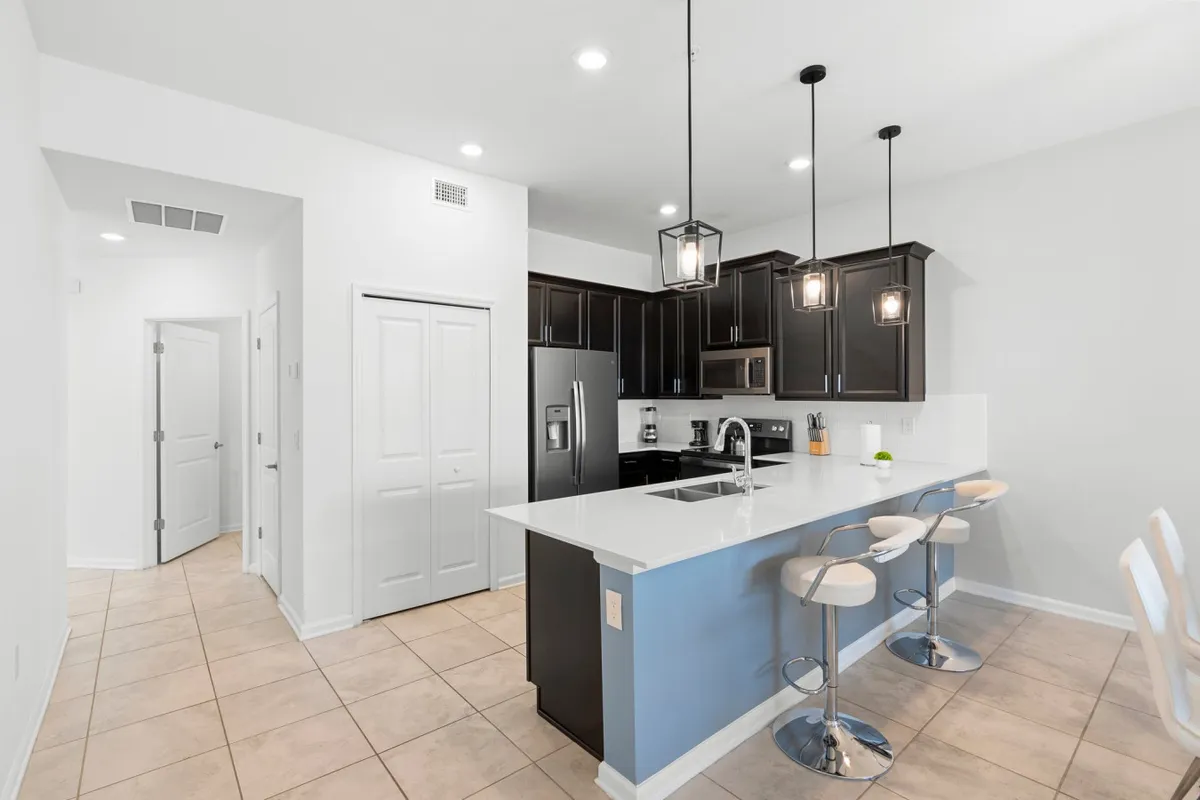 A welcoming, contemporary kitchen with a central island, bar stools, pendant lighting, and gleaming stainless steel appliances. The space is designed for both serious cooking and lively conversation, blending function with style.