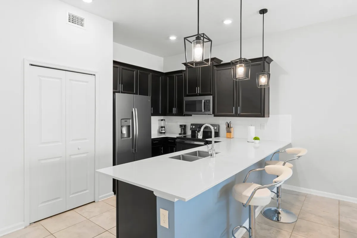 A sophisticated and cozy kitchen scene featuring an island countertop, stainless steel appliances, pendant lights, and bar stools. The setup highlights both cooking facilities and a breakfast bar, inviting casual dining and social interaction.